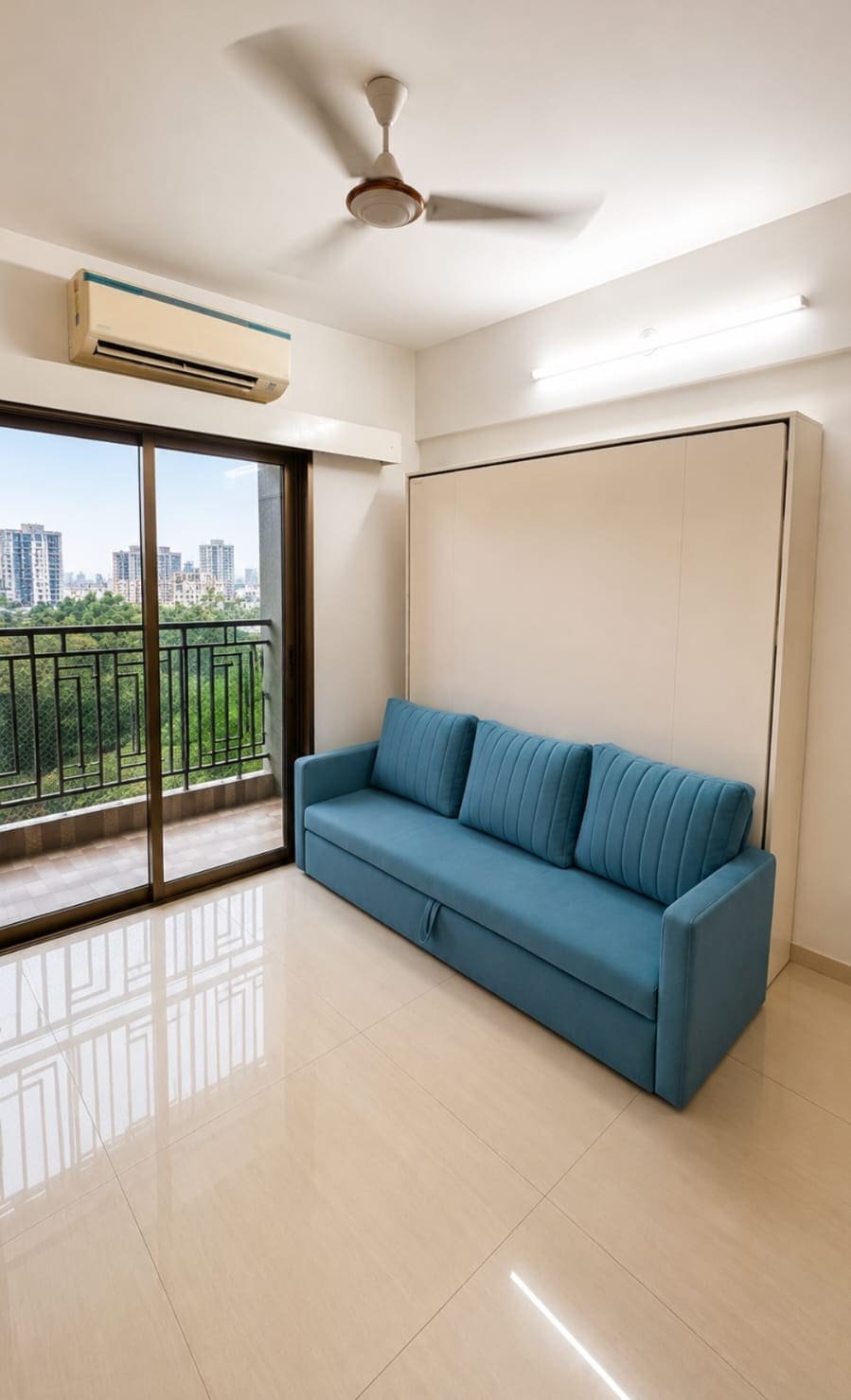 Day mode: a white Dwalsbed closed flush to the wall with a teal three-seater sofa in front, in a bright Mumbai flat with a balcony view.