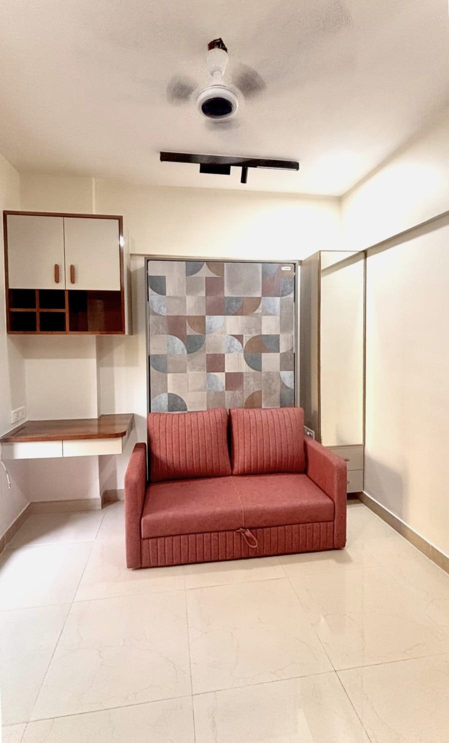 4×6 Dwalsbed with a geometric-print door, rust two-seater sofa in front, side dressing unit and a wall-mounted desk in a compact Mumbai bedroom.